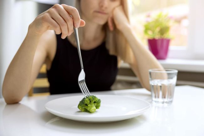dieting problems, eating disorder – unhappy woman looking at small broccoli portion on the plate eating disorder warning signs and tips