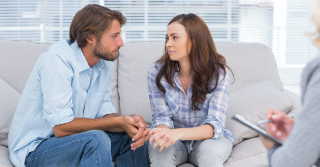 Couple looking to each other during therapy session while therapist watches couples therapy