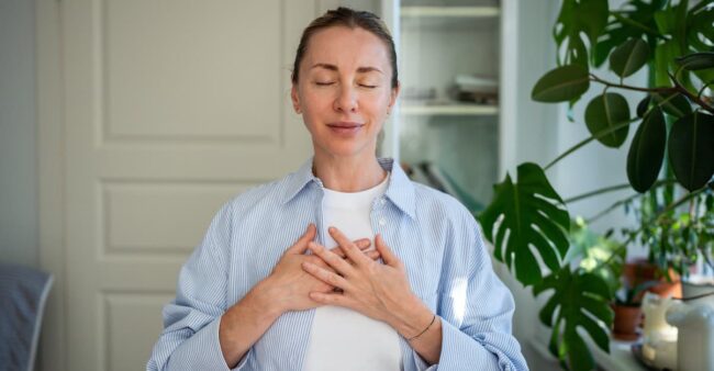 Peaceful woman standing with closed eyes, folding one’s arms on chest doing breathing exercises. stress free daily routine
